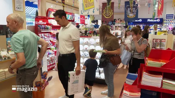 Erwachsene und Kinder, die in einem Schreibwarenladen vor der Kasse stehen.