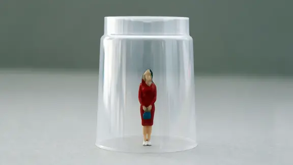 Eine Miniaturfigur steht unter einem Plastikbecher