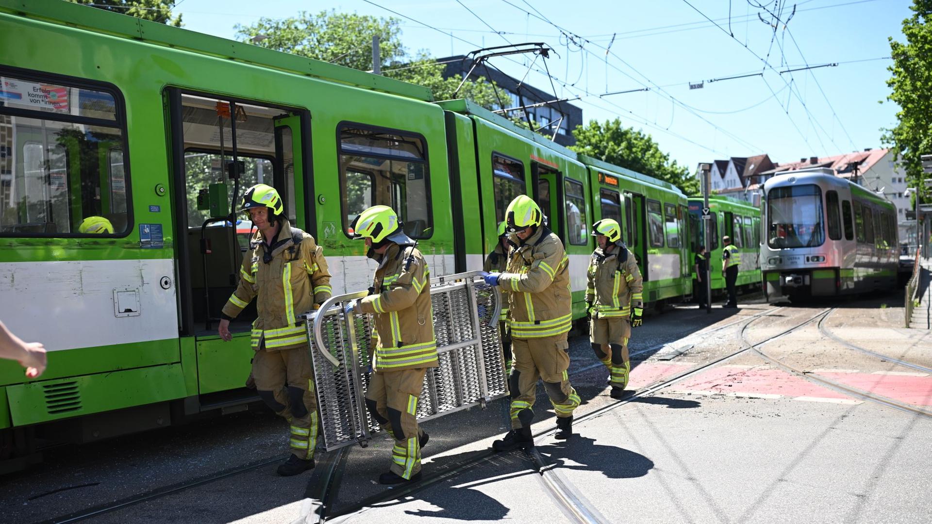 Feuerwehrleute laufen nach einem Unfall mit Hilfsgerät an einer Stadtbahn entlang. | dpa, Julian Stratenschulte