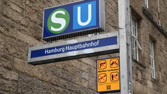 Ein gelbes Schild, das auf das geltende Waffenverbot hinweist, hängt unter dem Eingangsschild am Hamburger Hauptbahnhof neben den Logos von S-Bahn und U-Bahn.