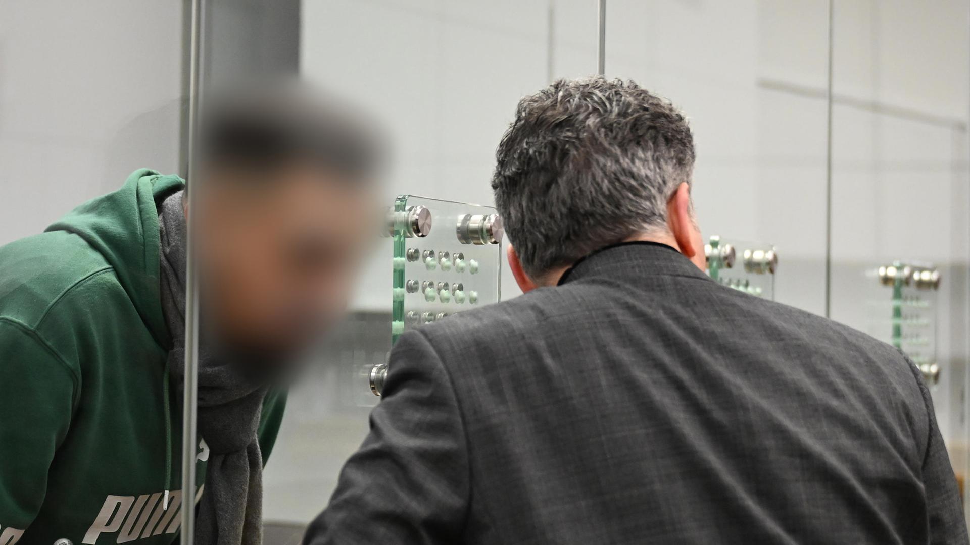 Der Angeklagte (l), mutmaßliches Mitglied der Hisbollah, steht im Oberlandesgericht hinter einer Glaswand. | picture alliance/dpa, Shireen Broszies