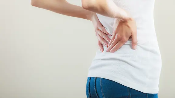 Eine Frau hält sich den unteren Rücken.