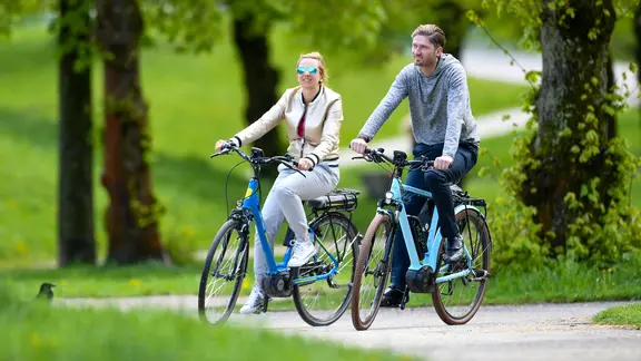 Ein Paar fährt mit Pedelecs durch einen Park.