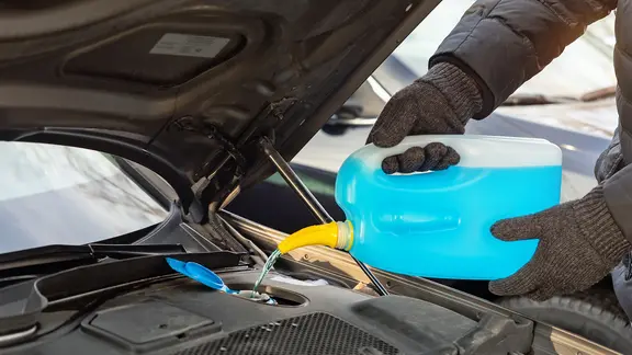 Hände mit Handschuhen gießen Frostschutz in eine Öffnung im Motorraum eines Autos