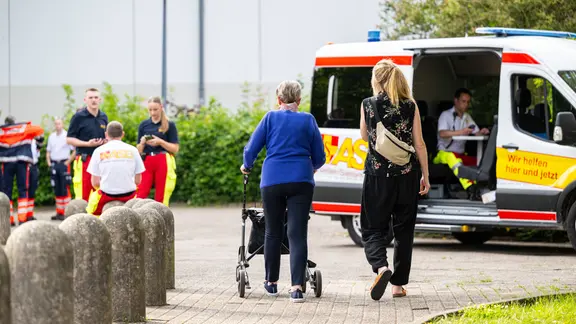 Eine Frau begleitet eine ältere Dame mit Rollator zum Evakuierungszentrum.