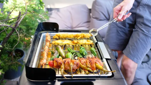 Ein Mann steht an einem Elektrogrill auf einem Balkon.