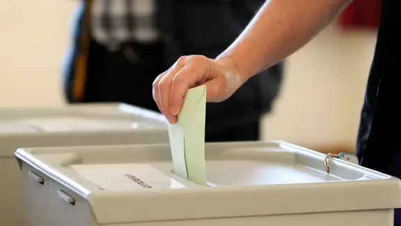 Jemand wirft einen Zettel in eine Wahlurne.
