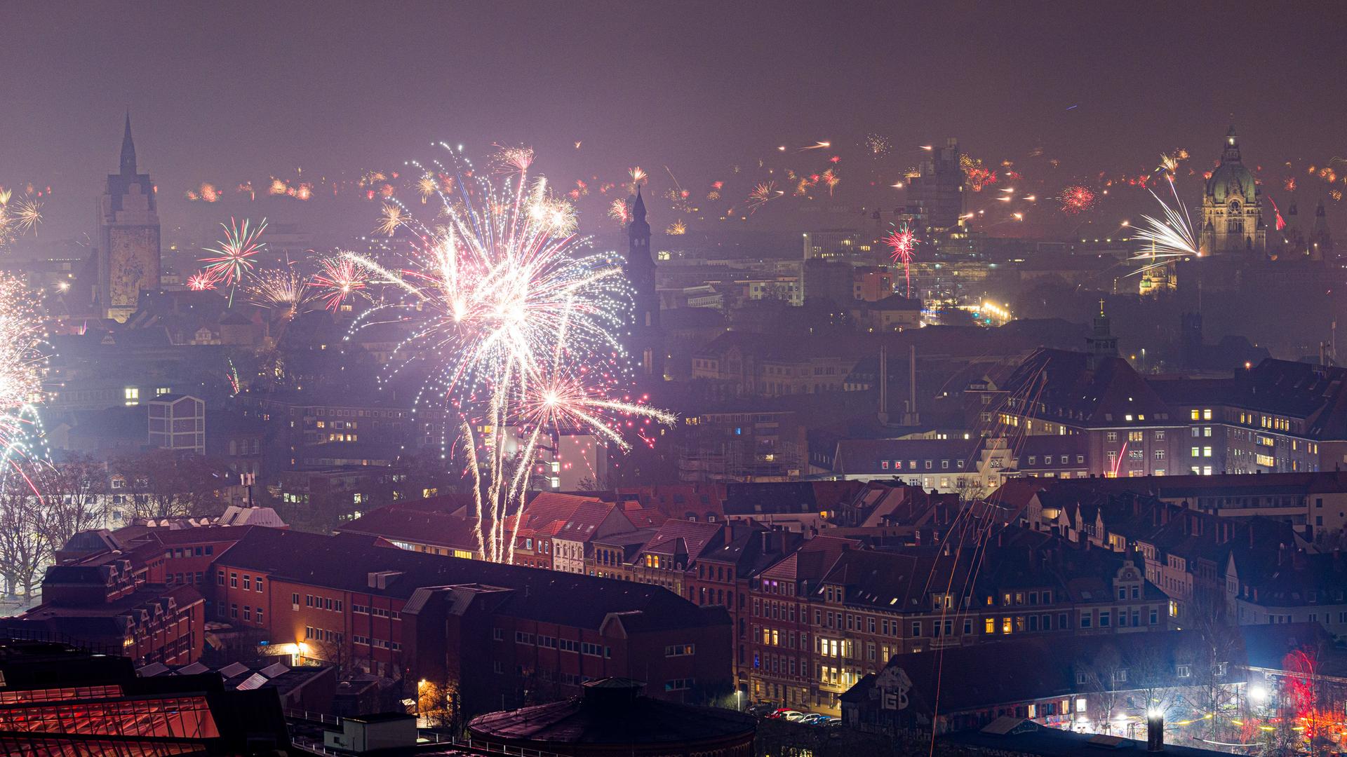 Feuerwerk explodiert in der Silvesternacht am Himmel neben der Marktkirche und dem Neuen Rathaus in Hannover. | Moritz Frankenberg/dpa +++ dpa-Bildfunk +++