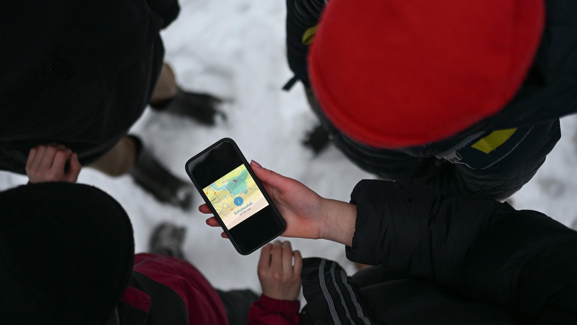 Vier Schüler blicken auf ein Smartphone, das den Schulausfall für den Landkreis Leer anzeigt. | picture alliance/dpa | Lars Penning