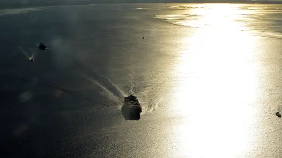 Luftaufnahme eines Containerschiffs im Gegenlicht der Abendsonne bei Einfahrt in die Elbe.