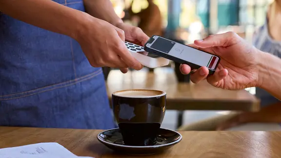 Eine Person zahlt in einem Café mit seinem Smartphone. | picture alliance / Shotshop , Monkey Business 2 Eine Person zahlt in einem Café mit seinem Smartphone.