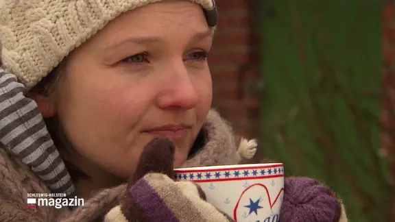 Eine Frau mit Mütze trinkt eine Tasse Tee.