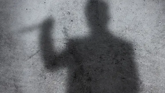 Silhouette eines Mannes der mit einem Messer droht vor einer Steinwand.
