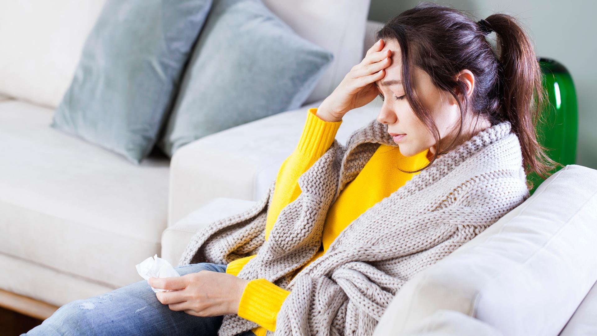 Eine kranke Frau sitzt auf einem Sofa und fasst sich an die Stirn. | Colourbox, Ahmet Eylem Misirligül