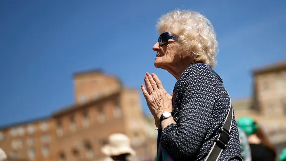 Eine alte Frau betet auf dem Petersplatz