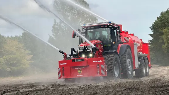 Ein rotes Feuerwehrauto mit rotem Anhänger und Wasserspritzern.