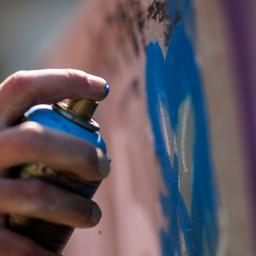Jemand sprüht mit einer Spraydose ein Graffiti an eine Wand.