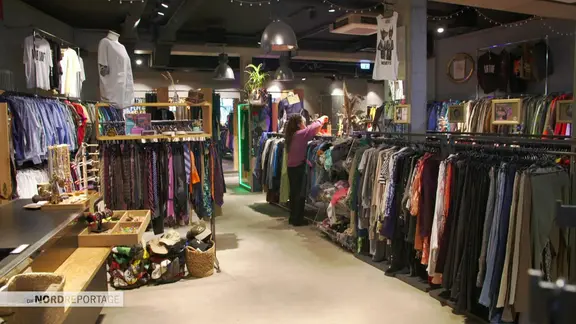 Kleidungstücke liegen in einem Secondhandladen aus.