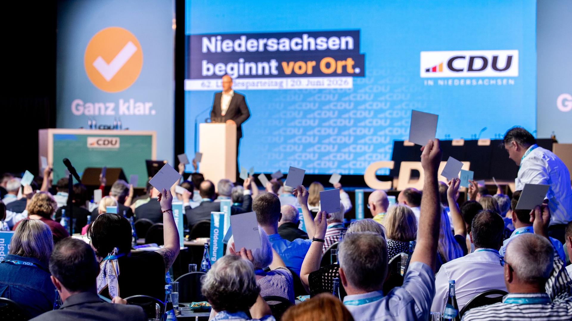 Menschen halten Stimmzettel hoch vor einer Bühne auf dem CDU-Landesparteitag in Vechta. | dpa-Bildfunk, Hauke-Christian Dittrich