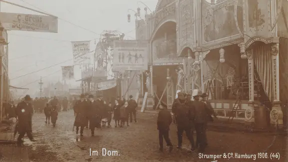 Ein historisches Bild vom Hamburger Dom 1906, Menschen in Winterkleidung gehen an Ständen entlang.