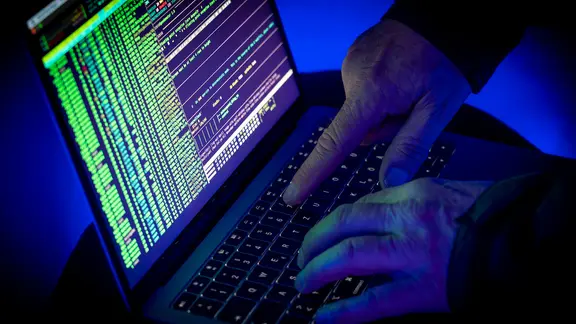 Eine Person in einem dunklen Raum tippt etwas in einen Laptop ein.