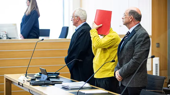 Ein Angeklagter (Mitte) steht neben seinem Verteidiger Matthias Jochmann (links) im Landgericht Braunschweig. | dpa, Moritz Frankenberg Ein Angeklagter (Mitte) steht neben seinem Verteidiger Matthias Jochmann (links) im Landgericht Braunschweig.