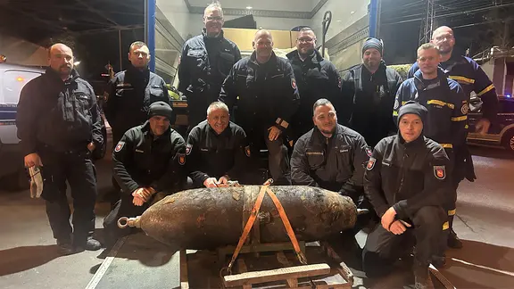Mehrere Mitglieder des Kmapfmittelräumdienstes stehen zum Gruppenbild rund um einen entschärften Blindgänger vor einem Transporter.