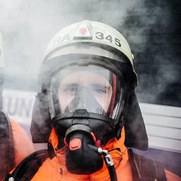 Zwei Feuerwehrleute mit Atemschutzmasken sind von Rauch umhüllt.