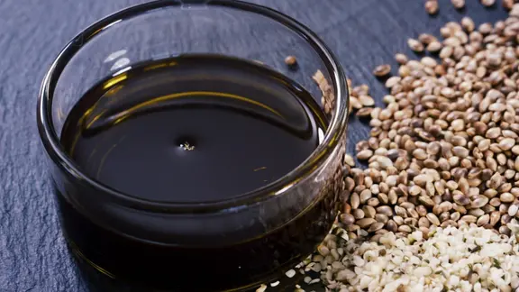 Hanfsamen liegen neben einer Schale Hanföl auf einer Schieferplatte. | Screenshot Hanfsamen liegen neben einer Schale Hanföl auf einer Schieferplatte.