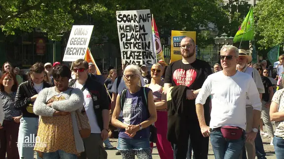 Mehrere Menschen haben sich in bunten Farben und mit Plakaten bei einer Kundgebung gegen die AfD auf einem Platz versammelt.