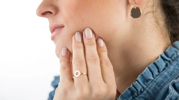 Frau greift sich an ihr Kiefergelenk.