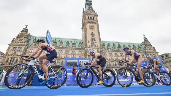 Teilnehmerinnen des Triathlons fahren mit dem am Hamburger Rathaus vorbei.