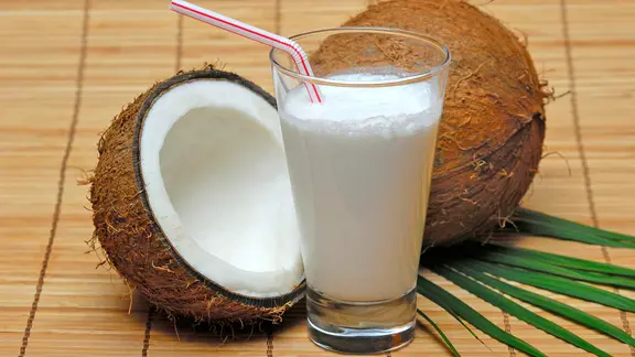 Ein Glas mit Kokosmilch, dahinter eine aufgeschnittene Kokosnuss.