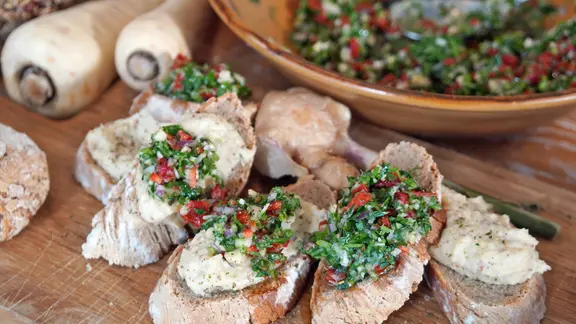 Mit Pastinaken-Creme und Petersilien-Pesto bestrichene Brote auf einem Holzbrett.