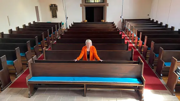 Pastorin Anne Mirjam Walter steht inmitten von Kirchenbänken.