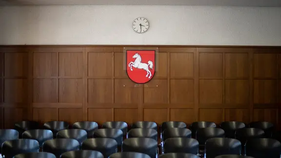 In einem Gerichtssaal hängt hinter mehreren Stuhlreihen das Wappen des Landes Niedersachsen.