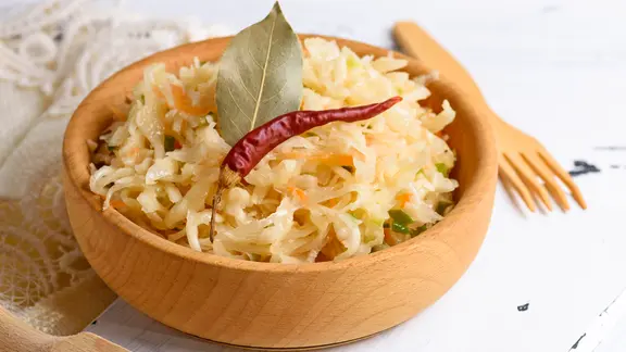 Eine Holzschale mit Sauerkraut, dekoriert mit einer Chilischote.