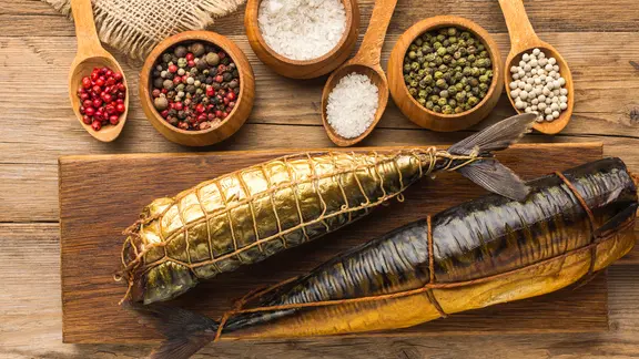 Zwei ganze geräucherte Fische und verschiedene Gewürze auf einem Holzbrett
