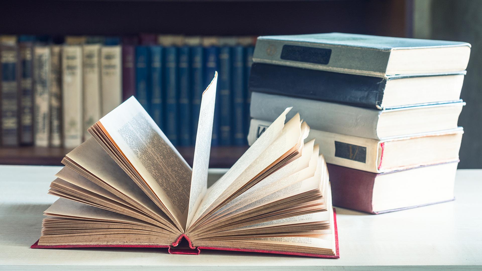 Bücher liegen auf einem Tisch vor einem Bücherregal. | Colourbox