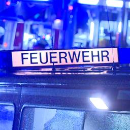 Ein Feuerwehr-Fahrzeug mit dem Schriftzug Feuerwehr steht bei Nacht vor einem Einsatzort, im Hintergrund sind Feuerwehrleute zu sehen.