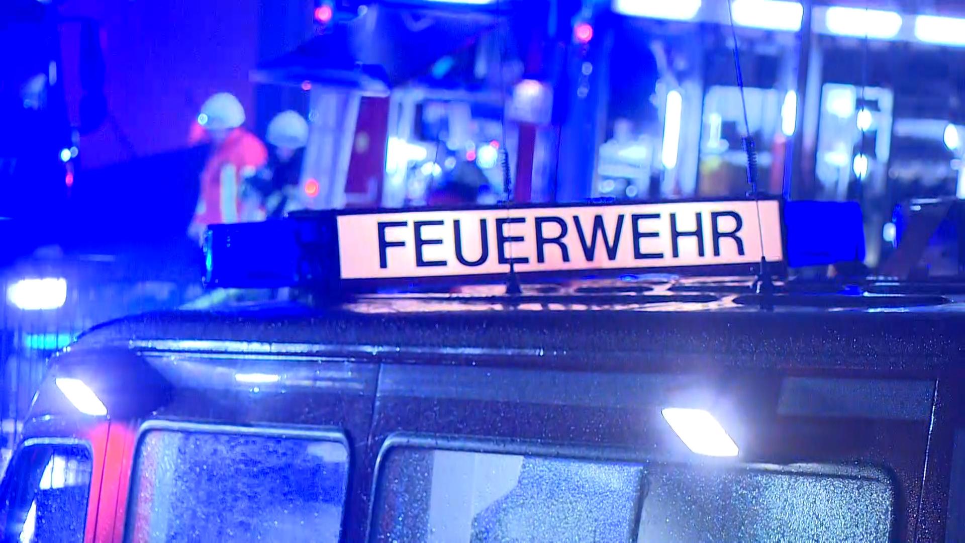 Ein Feuerwehr-Fahrzeug mit dem Schriftzug Feuerwehr steht bei Nacht vor einem Einsatzort, im Hintergrund sind Feuerwehrleute zu sehen. | NonstopNews