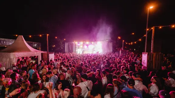 Eine große Menschenmenge steht nachts vor einer hell erleuchteten Bühne. Auf der Bühne findet ein Konzert statt.
