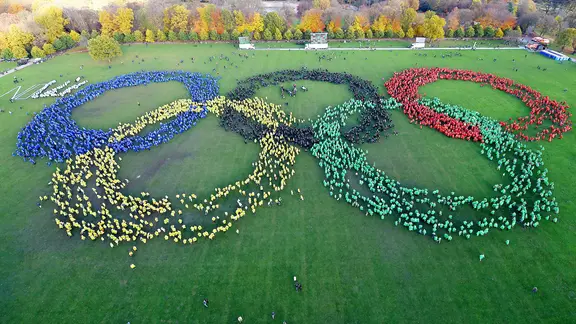 Die olympischen Ringe und ein Schriftzug "No" auf einer grünen Wiese.