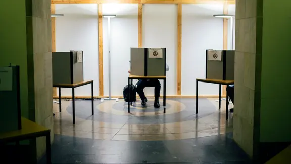 Ein Mann sitzt in einer kleinen Wahlkabine. | Julius Matuschik Ein Mann sitzt in einer kleinen Wahlkabine.