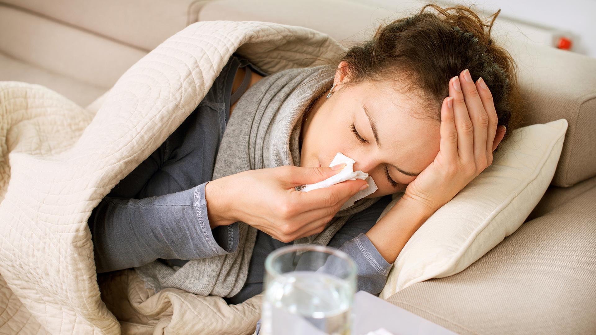Kranke Frau liegt auf einem Sofa und schnäuzt sich die Nase. | Fotolia, Subbotina Anna