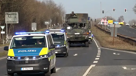 Ein Konvoi von Militärfahrzeugen wird von der Polizei auf einer Straße begleitet.