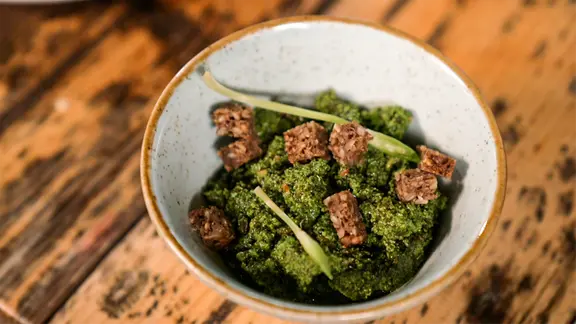 Ein Schälchen mit Spinat-Bärlauch-Pesto steht auf einem Tisch.