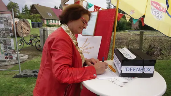 Eine Frau unterschreibt ein Formular für einen Ideenwettbewerb.