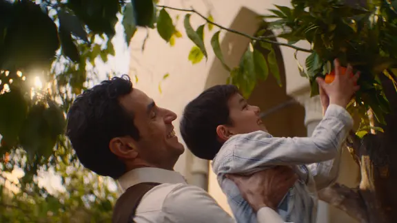 Szene aus dem Film "Im Schatten des Orangenbaums": Ein Mann hebt einen kleinen Jungen, der eine Orange pflückt.