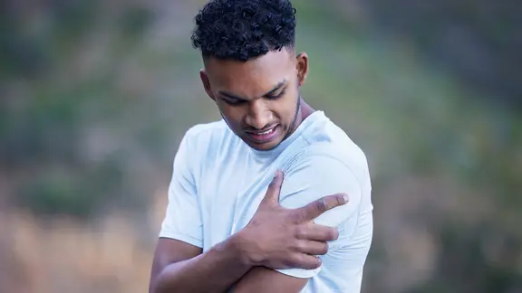 Impingement in der Schulter: Junger Mann fasst sich an die schmerzende Schulter.